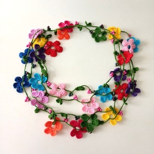 May include: A multi-strand crocheted necklace with colorful flower charms and green leaves. The necklace is made with small black beads.