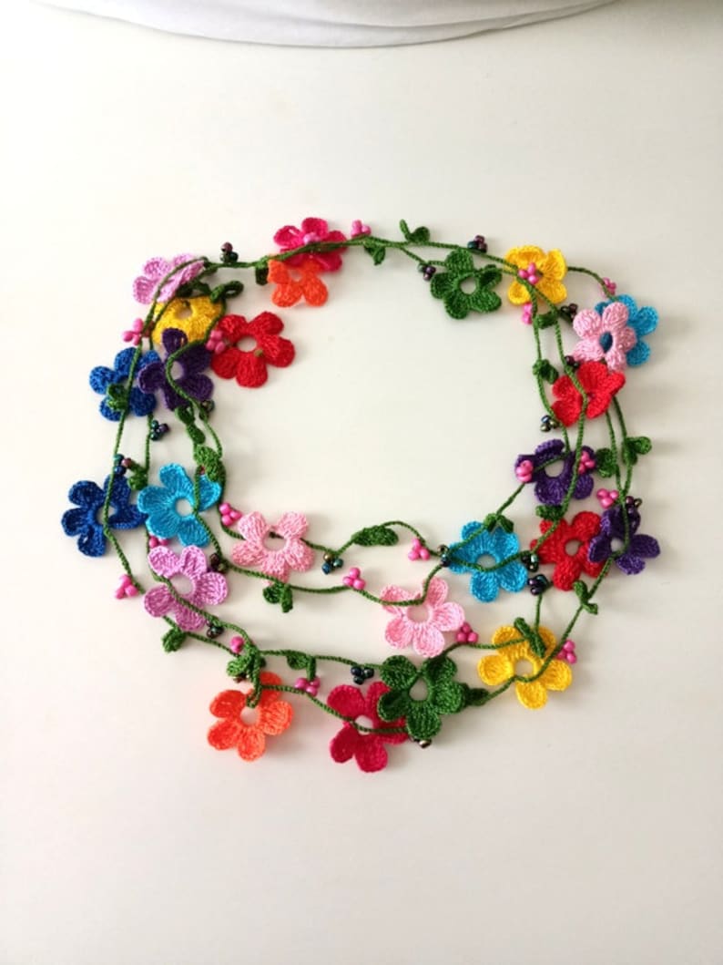 May include: A multi-strand crocheted necklace with colorful flower charms and green leaves. The necklace is made with small black beads.