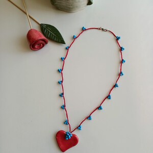 May include: A red heart-shaped pendant necklace with blue beads on a red cord.