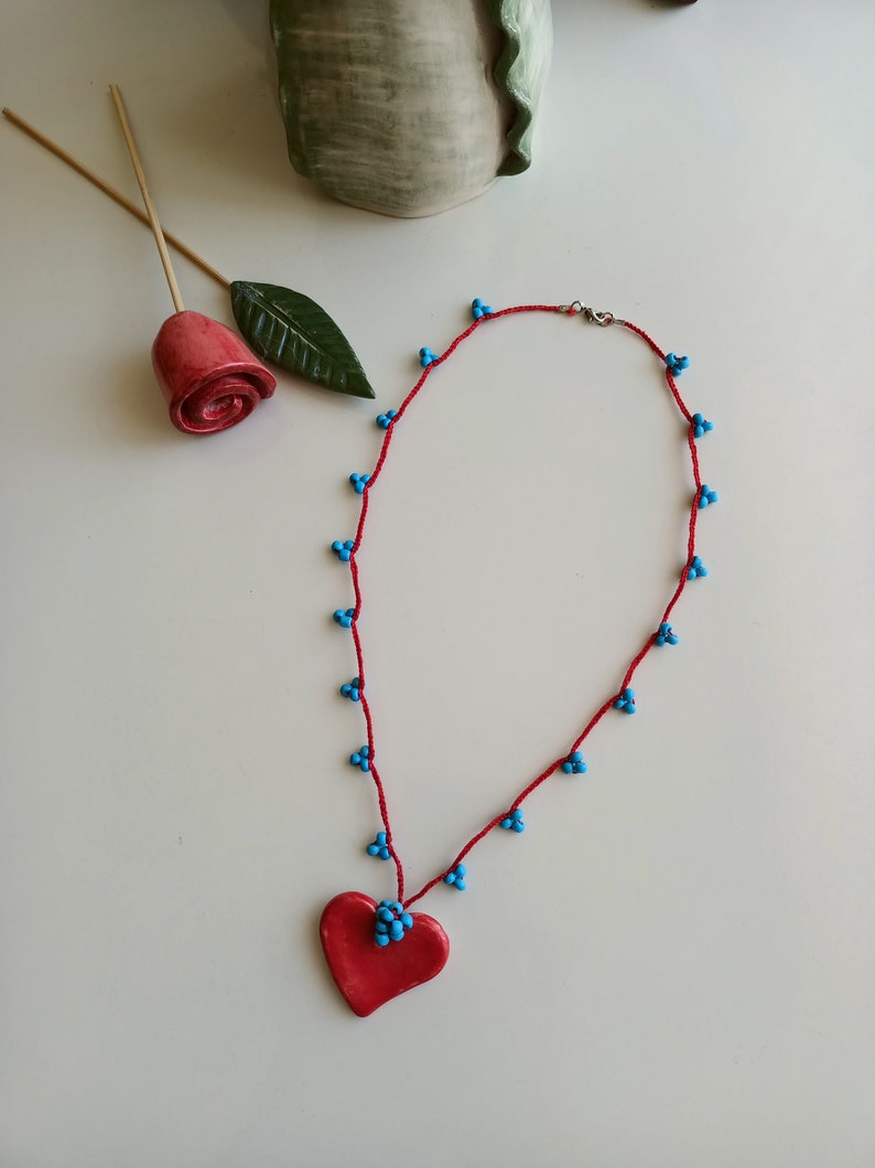 May include: A red heart-shaped pendant necklace with blue beads on a red cord.