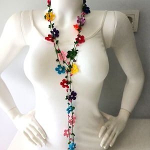 May include: A long, colorful crocheted necklace with small flower-shaped beads. The necklace is made with a variety of colors, including red, orange, yellow, green, blue, purple, and pink.