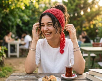 May include: A bright red crocheted headscarf featuring an openwork pattern and a small heart-shaped detail at the end. The headscarf is worn tied around the head, covering the hair with a textured, handmade appearance and a vibrant solid color.