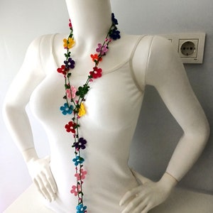 May include: A long, colorful crochet necklace with small flower-shaped beads. The necklace is made with green, pink, blue, yellow, red, and purple yarn.