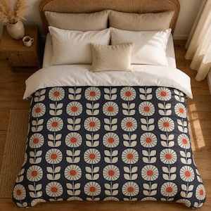 May include: A bedding set featuring a dark navy blue duvet cover with a repeating pattern of stylized cream-colored flowers with orange centers and stems. The set includes two large cream pillows and one smaller rectangular cream accent pillow.