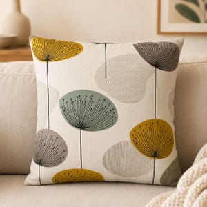 May include: A square throw pillow featuring an off-white background with a repeating pattern of stylized dandelion-like seed heads in mustard yellow, sage green, and charcoal gray, connected by thin black vertical lines and soft gray shapes.
