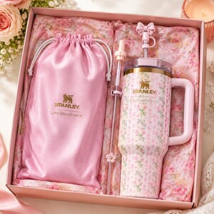 May include: A pink gift box containing a Stanley LoveShackFancy tumbler with a floral pattern, a matching pink satin drawstring pouch with the Stanley LoveShackFancy logo, and a clear straw featuring a small pink bow and flower charm topper.