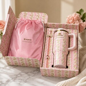 May include: A Stanley and LoveShackFancy collaboration set featuring a pink floral tumbler with a handle, a matching straw, and a pink satin drawstring bag. The items are presented in a floral patterned box with the Stanley and LoveShackFancy logos.