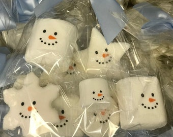 Op de afbeelding: Witte marshmallowtraktaties in de vorm van sneeuwpoppen, sterren en sneeuwvlokken, elk voorzien van een handgetekende zwarte stippellach, zwarte ogen en een oranje wortelneus. Individueel verpakt in doorzichtig plastic met een lichtblauw lint.