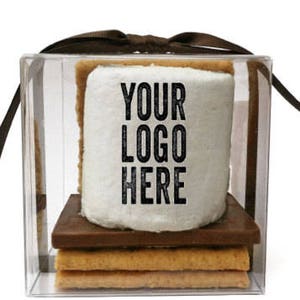 May include: A s'more treat in a clear box tied with a brown ribbon. The s'more includes graham crackers, a chocolate square, and a large marshmallow with the text "YOUR LOGO HERE" printed on it.
