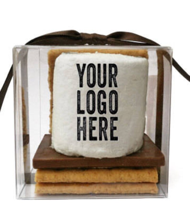 May include: A s'more treat in a clear box tied with a brown ribbon. The s'more includes graham crackers, a chocolate square, and a large marshmallow with the text "YOUR LOGO HERE" printed on it.