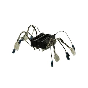 May include: A spider-shaped sculpture constructed from a black rectangular integrated circuit component with multiple legs made of twisted silver-coloured wire, each tipped with a small blue and black cylindrical electronic resistor component.