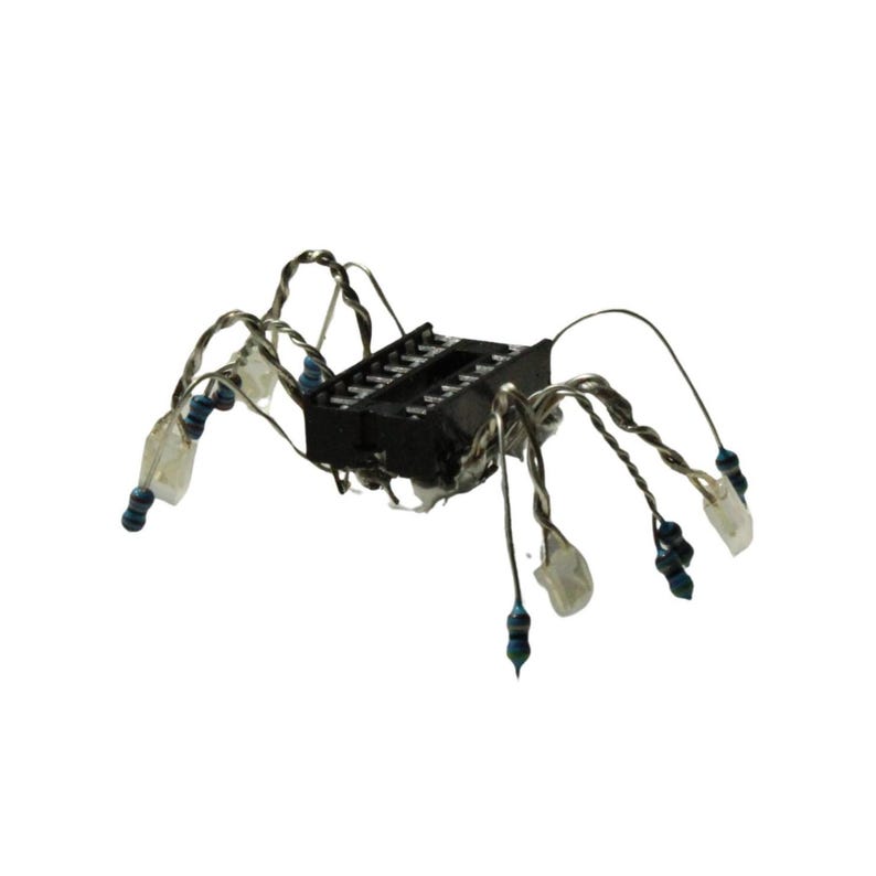 May include: A spider-shaped sculpture constructed from a black rectangular integrated circuit component with multiple legs made of twisted silver-coloured wire, each tipped with a small blue and black cylindrical electronic resistor component.