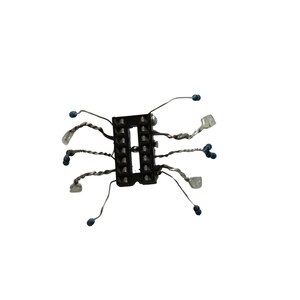 May include: A black rectangular electronic component socket with two parallel rows of pin slots. Several thin, twisted silver-coloured metal wires extend outward from the sides, each tipped with a small blue bead or a clear, translucent rectangular component.