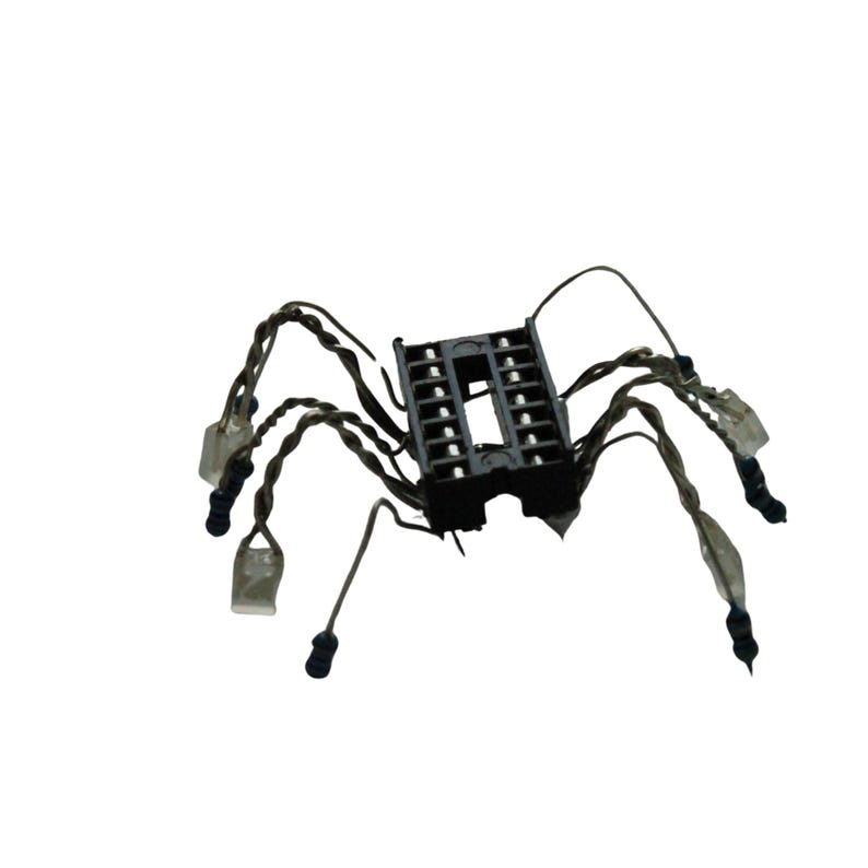 May include: A black electronic integrated circuit socket with eight twisted wire legs extending outwards. Each wire leg features a small, clear plastic component at the tip, resembling a mechanical spider-like structure made from electronic parts.
