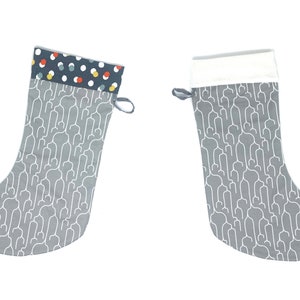 May include: Two Christmas stockings. One has a grey background with a white stethoscope pattern and a cuff with a navy blue background and colourful polka dots. The other stocking has a white cuff.