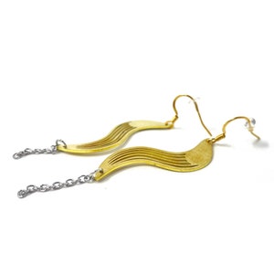 May include: A pair of gold earrings with a wavy, geometric design. The earrings are attached to a silver chain.