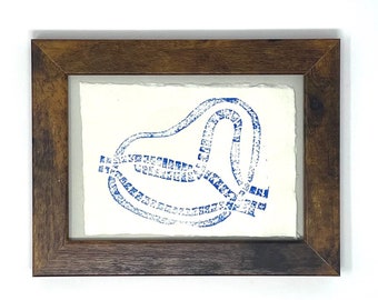 May include: Abstract blue print art in a dark brown wooden frame. The artwork features a blue, looping design on a white background. The frame has a natural wood grain finish, adding a rustic touch to the piece. The artwork is a unique decorative item.