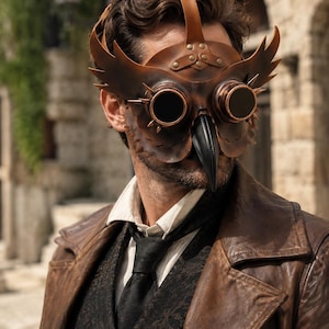 Può includere: Una maschera da gufo in pelle marrone con occhiali circolari integrati, bordi color rame e piccole punte. La maschera presenta un prominente becco nero, pannelli laterali decorativi a forma di ala e un cinturino in pelle con rivetti.