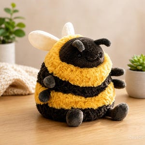Pode incluir: Um brinquedo de pelúcia em forma de abelha com um corpo redondo e felpudo, apresentando listras horizontais alternadas em preto e amarelo. O bicho de pelúcia tem duas pequenas asas brancas nas costas, antenas escuras e quatro pequenos membros.