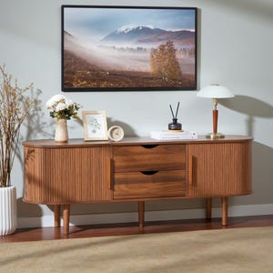 May include: A long, oval-shaped wooden sideboard featuring two central drawers with cutout handles and two side cabinets with vertical slatted doors. The piece is supported by six tapered wooden legs and has a warm, medium-brown wood grain finish.