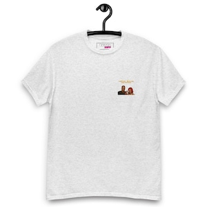 Op de afbeelding: Een lichtgrijs gemêleerd T-shirt met korte mouwen en een kleine afbeelding op de linkerborst. De afbeelding toont twee personen en de gele tekst "LESLEY GORE" en "YOU DON'T OWN ME". Het T-shirt heeft een ronde hals en hangt aan een zwarte hanger.
