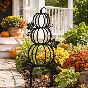 Könnte beinhalten: Ein schwarzer Gartenstecker aus Metall mit einem vertikalen Stapel aus drei stilisierten Kürbissen. Das Design umfasst dekorative Blatt- und Rankenausschnitte an den Seiten der Kürbisse. Der Stecker hat zwei Zinken zur Bodenbefestigung.