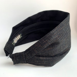 K&ouml;nnte beinhalten: Ein schwarzes und braunes Stoffhaarband mit einem Knotendesign. Das Haarband ist aus einem weichen, strukturierten Stoff.