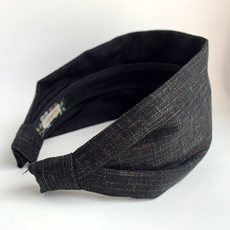 K&ouml;nnte beinhalten: Ein schwarzes und braunes Stoffhaarband mit einem Knotendesign. Das Haarband ist aus einem weichen, strukturierten Stoff.
