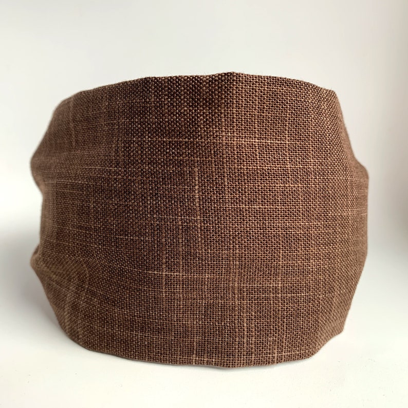May include: A brown linen face mask. The mask is made of a soft, breathable fabric and has a simple, rectangular shape.