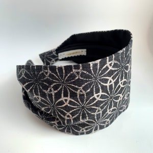 以下が含まれることがあります： 白い幾何学模様の黒いヘッドバンド。ヘッドバンドは布製で、頭に巻いて着用するように設計されています。