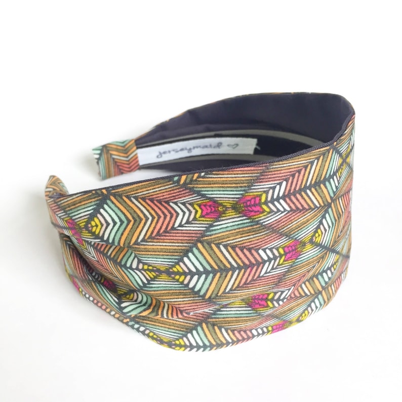 May include: A wide headband with a colorful geometric pattern in shades of orange, pink, green, and white. The interior is a dark navy blue. The text "jerseymade" is visible on the inside.