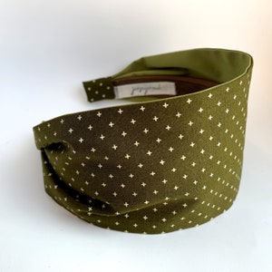 May include: A green headband with a white plus sign pattern. The headband is made of fabric and has a knotted design.