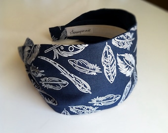 May include: A navy blue headband with a white feather pattern. The headband has a white label with the text "Jerseymail" on it.