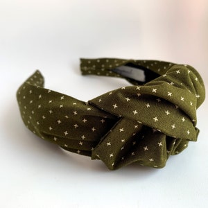 May include: A green headband with a white cross pattern. The headband is knotted and has a fabric texture.