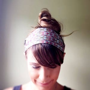 May include: A colorful headband with a geometric feather pattern in shades of pink, purple, and green. The headband is worn around the head, with the hair styled in a bun. The accessory adds a stylish touch to any hairstyle.