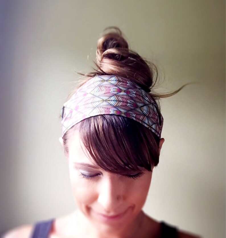 May include: A colorful headband with a geometric feather pattern in shades of pink, purple, and green. The headband is worn around the head, with the hair styled in a bun. The accessory adds a stylish touch to any hairstyle.