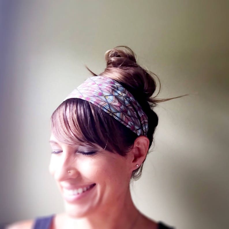May include: A colorful patterned headband in shades of pink, purple, and blue is worn on the head. The headband is wrapped around the forehead and is paired with a hairstyle that includes bangs and a bun. The person is smiling.