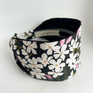 May include: Black headband with a white floral pattern. The headband has a black velvet lining.