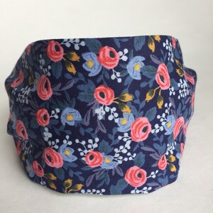 May include: A navy blue headband with a floral pattern. The fabric features pink roses, light blue flowers, and green leaves. The headband is a comfortable accessory for everyday wear.