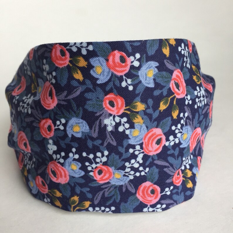 May include: A navy blue headband with a floral pattern. The fabric features pink roses, light blue flowers, and green leaves. The headband is a comfortable accessory for everyday wear.
