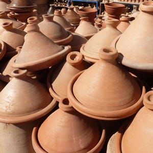 Peut inclure: Une collection de tajines en terre cuite non émaillée, dotés d'une base circulaire large et d'un couvercle conique surmonté d'un petit bouton. Ces récipients de cuisson traditionnels sont disposés en groupe, révélant leur texture d'argile.