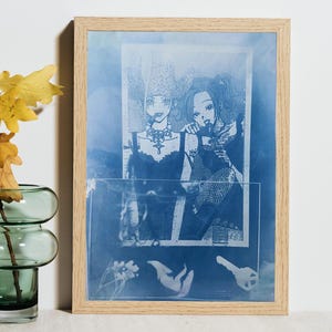 May include: A rectangular light wood frame containing a blue-toned cyanotype print. The artwork features a graphic illustration of two figures with detailed hairstyles and necklaces, layered with silhouettes of a key and small floral elements at the bottom.