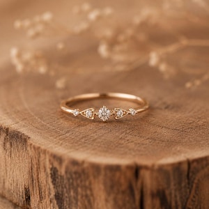 Puede incluir: Un anillo fino de oro con un diamante central de talla brillante redonda, flanqueado por dos engastes triangulares con un pequeño diamante cada uno, y dos diamantes redondos adicionales en los bordes exteriores del aro.