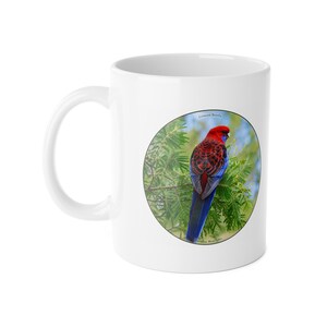 May include: A white ceramic mug featuring a circular graphic of a Crimson Rosella bird perched on a green pine branch. The bird has vibrant red, black, and blue feathers. The text Crimson Rosella and Paradise Bird Gifts is printed on the graphic.