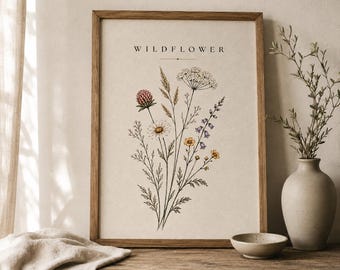 May include: A framed vertical wall art print featuring a botanical illustration of various wildflowers in muted tones of pink, yellow, and blue. The word WILDFLOWER is printed in black capital letters at the top centre of the off-white paper background.