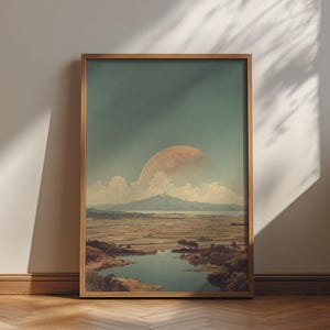 Op de afbeelding: Een ingelijste kunstdruk met een landschap met een grote, lichtoranje maan die opkomt boven een verre bergketen. Onder de berg strekt zich een uitgestrekt gebied van vlakke, gesegmenteerde velden uit naar een waterpartij op de voorgrond.