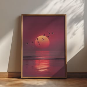 Könnte beinhalten: Ein gerahmter vertikaler Wandkunstdruck mit einem tiefroten und orangefarbenen Sonnenuntergang über einem ruhigen Meereshorizont. Ein Vogelschwarm ist vor der großen, leuchtenden Sonne abgebildet, mit Spiegelungen auf dem nassen Sand.