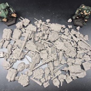 May include: A collection of unpainted grey plastic miniature robot parts and weapon components scattered in the center, flanked by two fully painted green and tan humanoid robot figurines standing on hexagonal bases at the top corners.