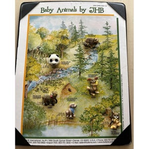 May include: A display card titled Baby Animals by JHB featuring six small animal-shaped buttons: a panda bear, a raccoon, a bear cub, a cottontail rabbit, a dog with a blue bandana, and a squirrel, all arranged on a printed forest landscape.