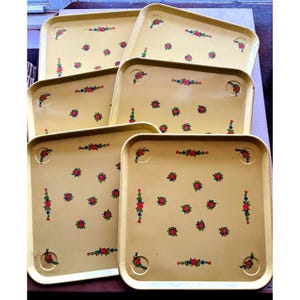 May include: A set of six rectangular serving trays in a pale yellow finish, each featuring a repeating pattern of small red roses with green leaves and blue accents. The trays have rounded corners and a smooth, flat surface for serving items.